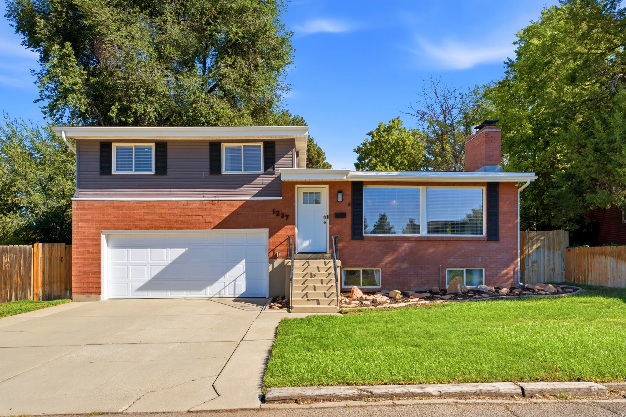 Brick and siding exterior featuring a two-car garage, front entry steps with handrail, and a manicured lawn with landscape rock accents