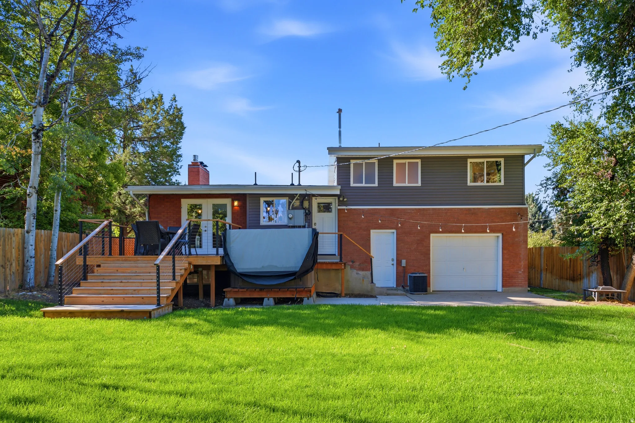 Expansive grassy area, multi-level wood deck with cable railing, red brick exterior, gray siding, and attached garage