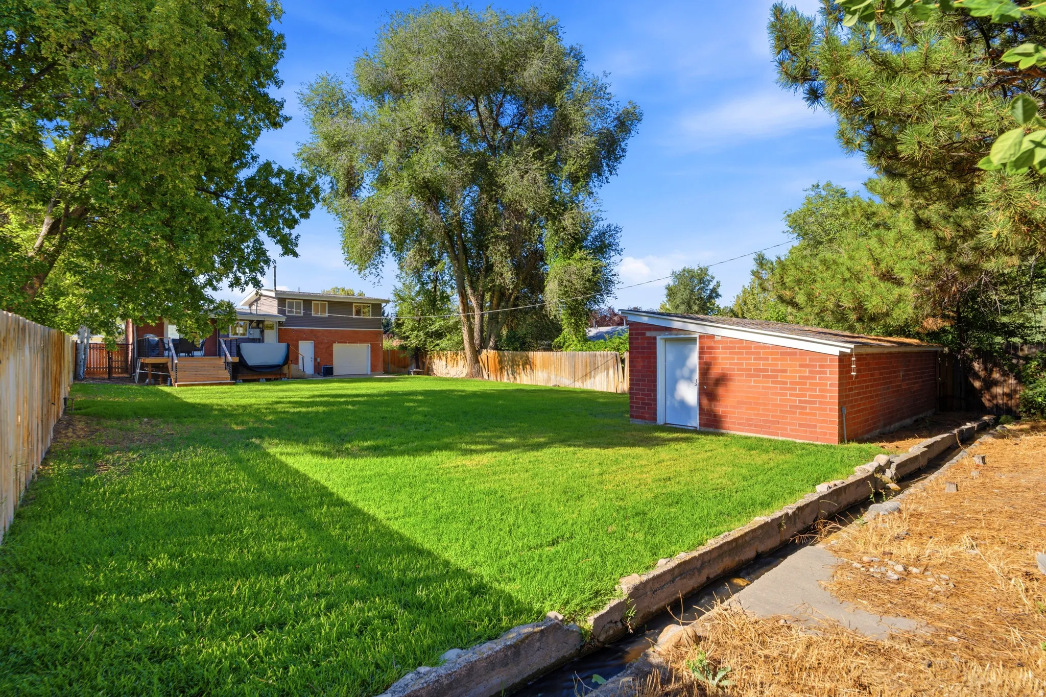 Expansive green lawn, mature trees, and a red brick storage shed