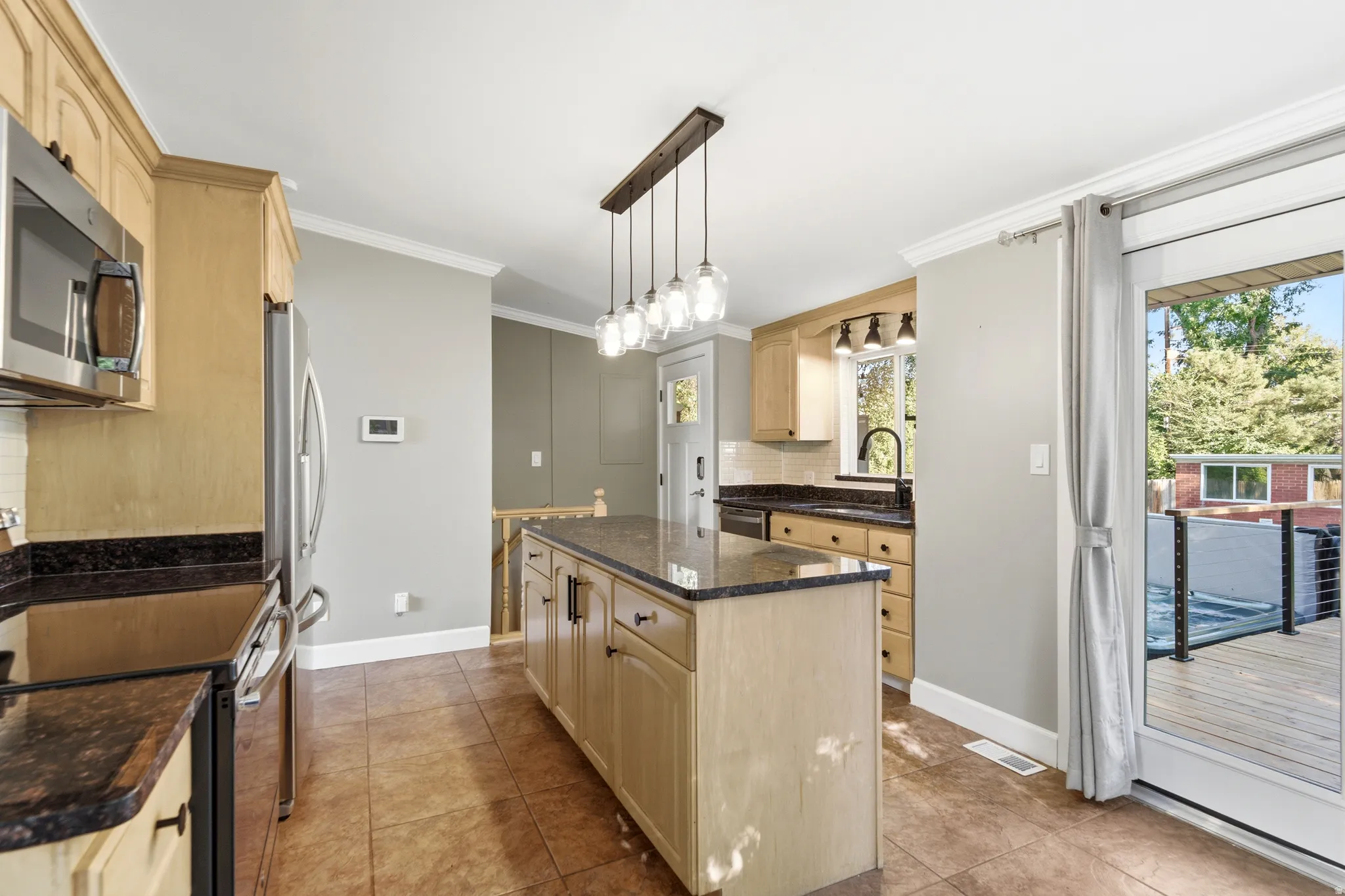 Kitchen featuring wood-finish cabinetry, stainless steel appliances, dark countertops, and a kitchen island with pendant lighting