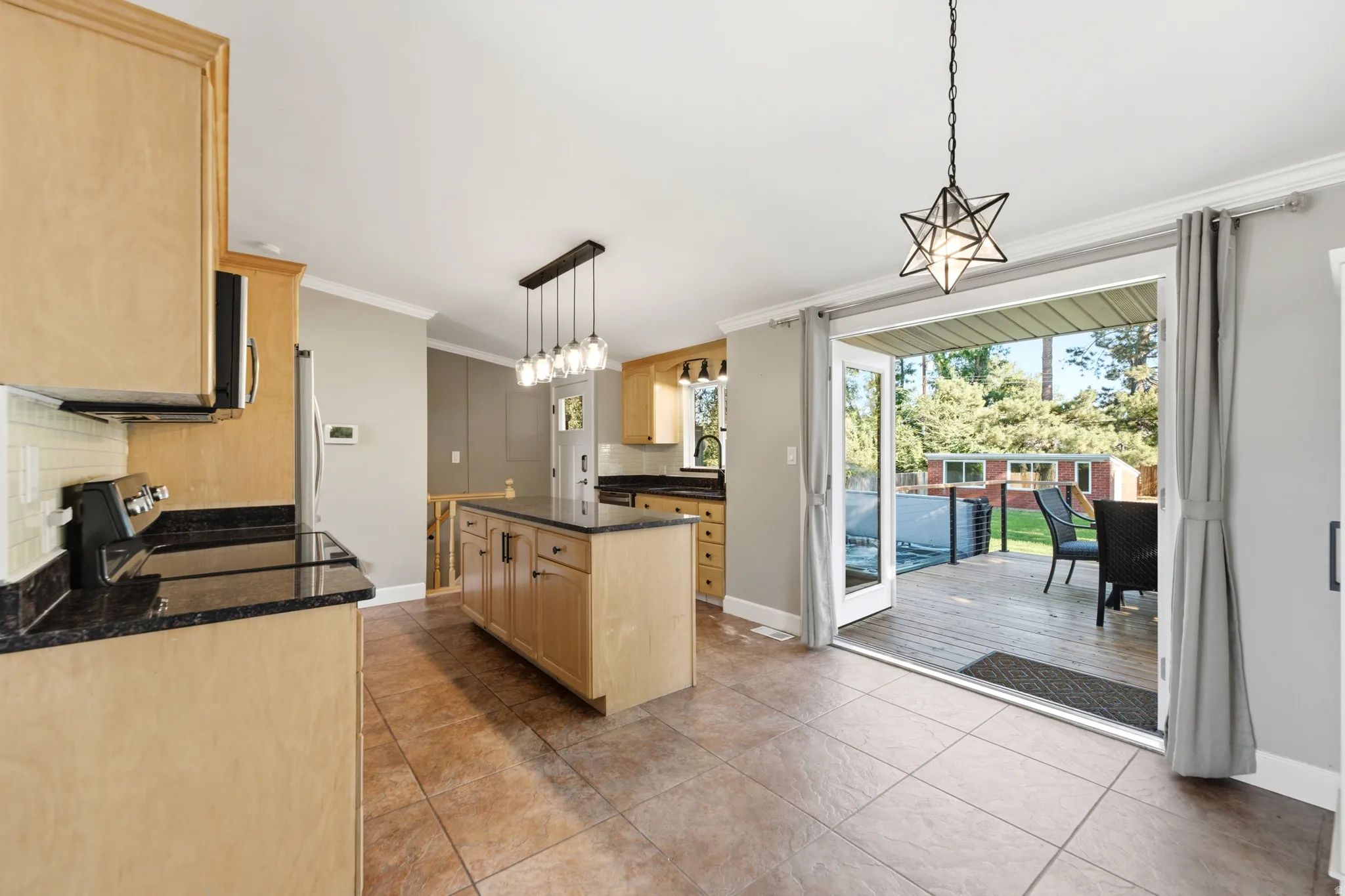 Kitchen featuring wood-finish cabinetry, black countertops, tile flooring, and a center island with pendant lighting