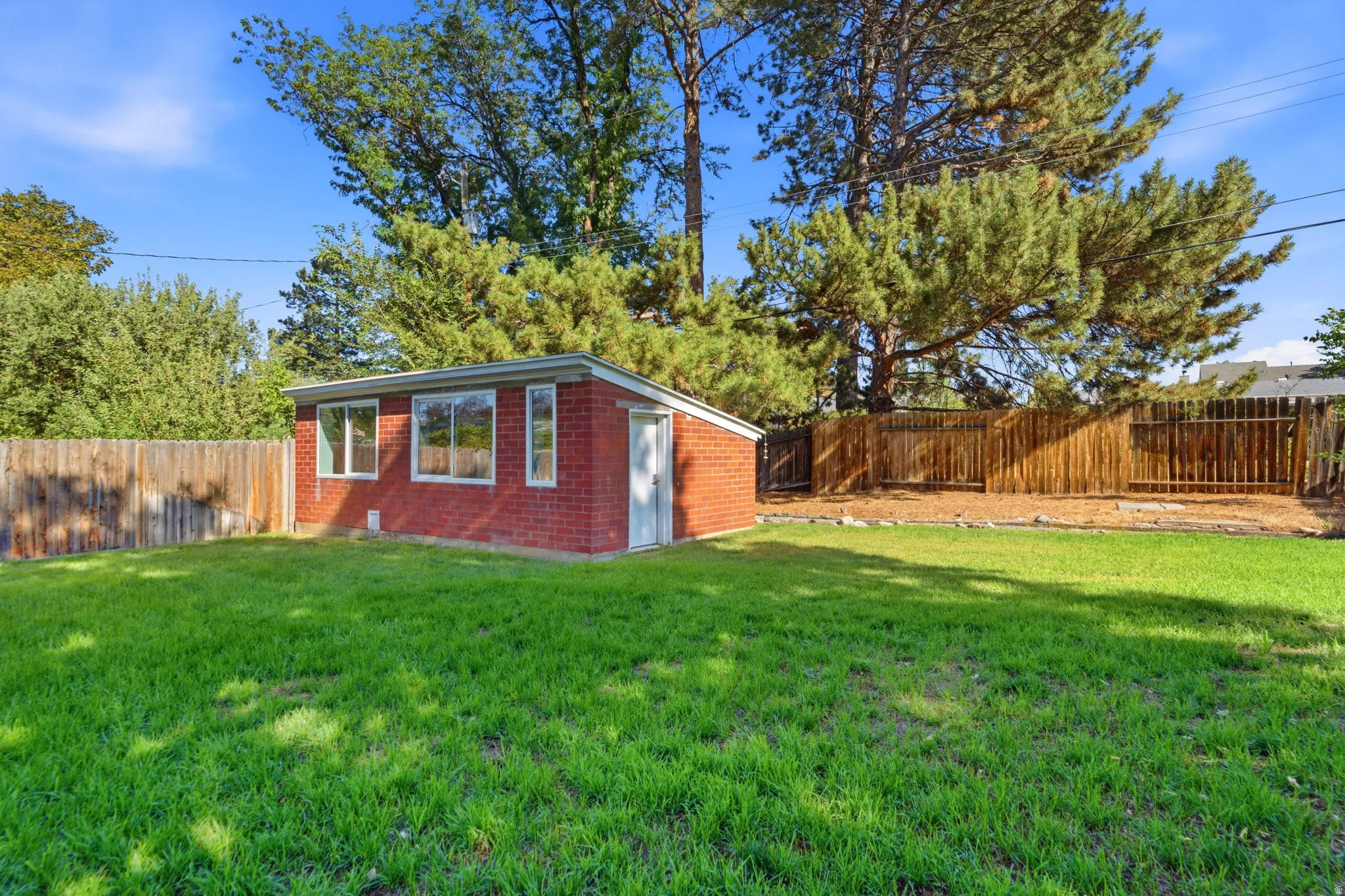 Expansive green lawn with a red brick outbuilding featuring multiple windows and a white door