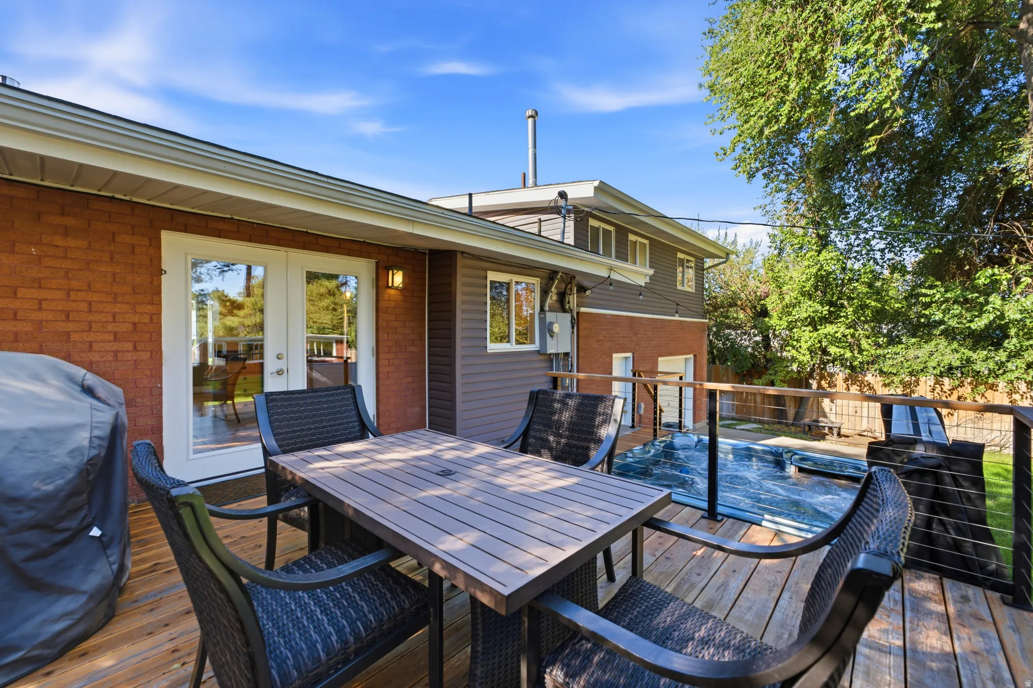 Spacious wood-finish deck with a built-in spa, contemporary metal railing, and direct access to the interior via French doors