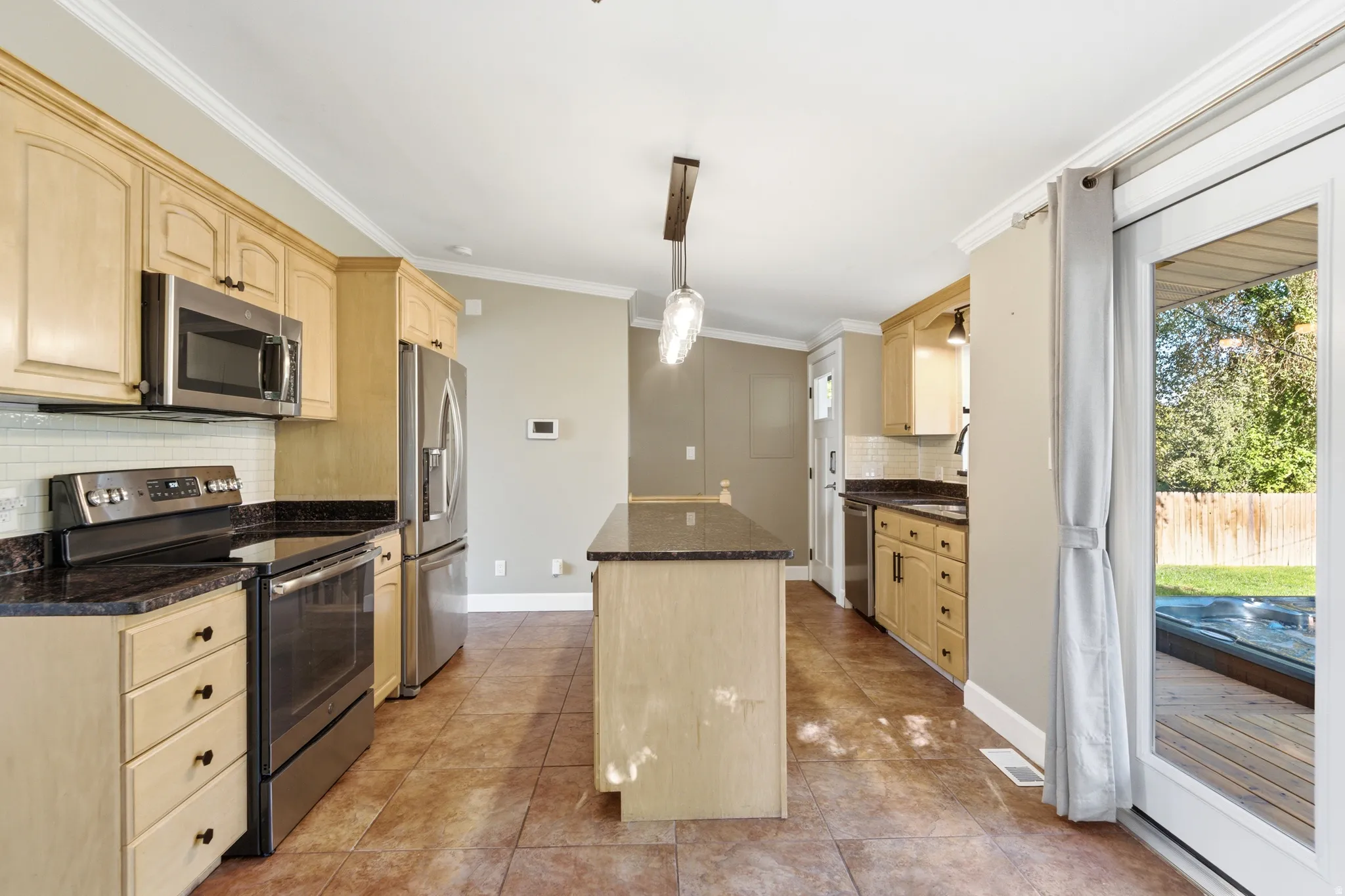 Kitchen featuring stainless steel appliances, dark countertops, a central island, and tiled flooring