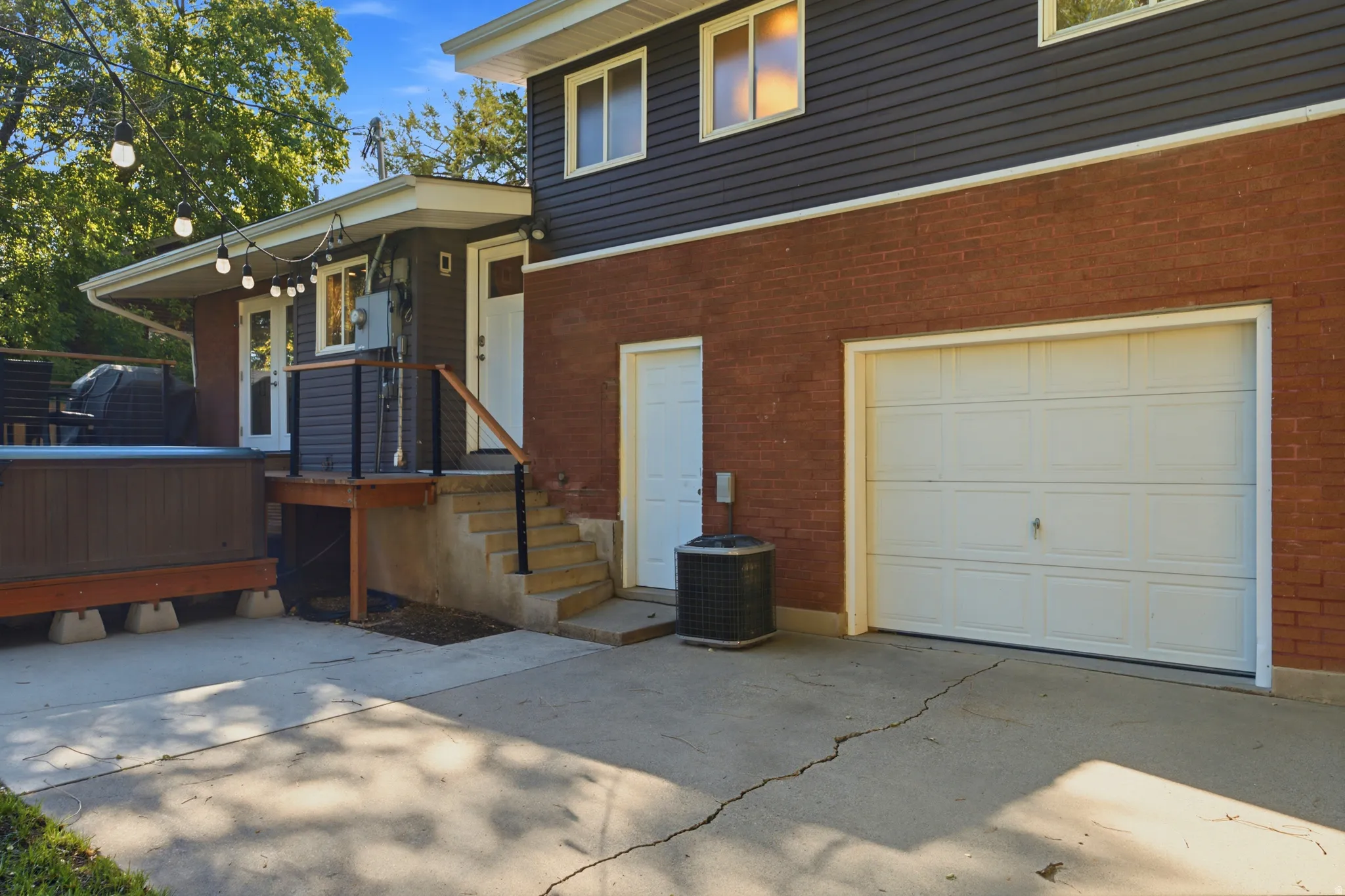 Brick and siding exterior with a garage, concrete patio, and exterior staircase with railing