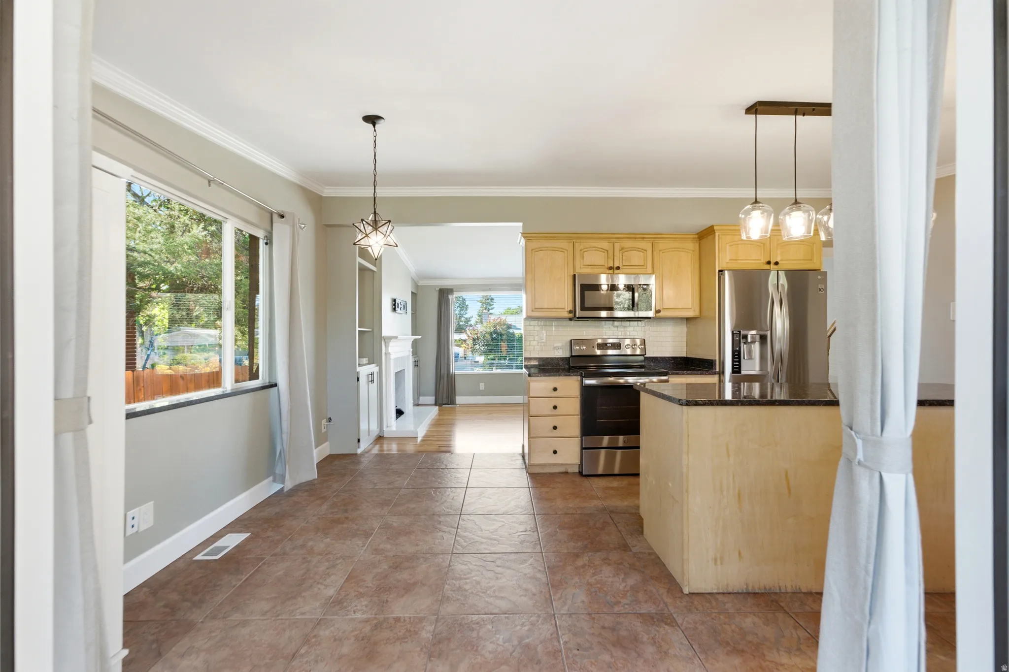 Kitchen featuring a center island, stainless steel appliances, light wood-finish cabinetry, and a tile backsplash