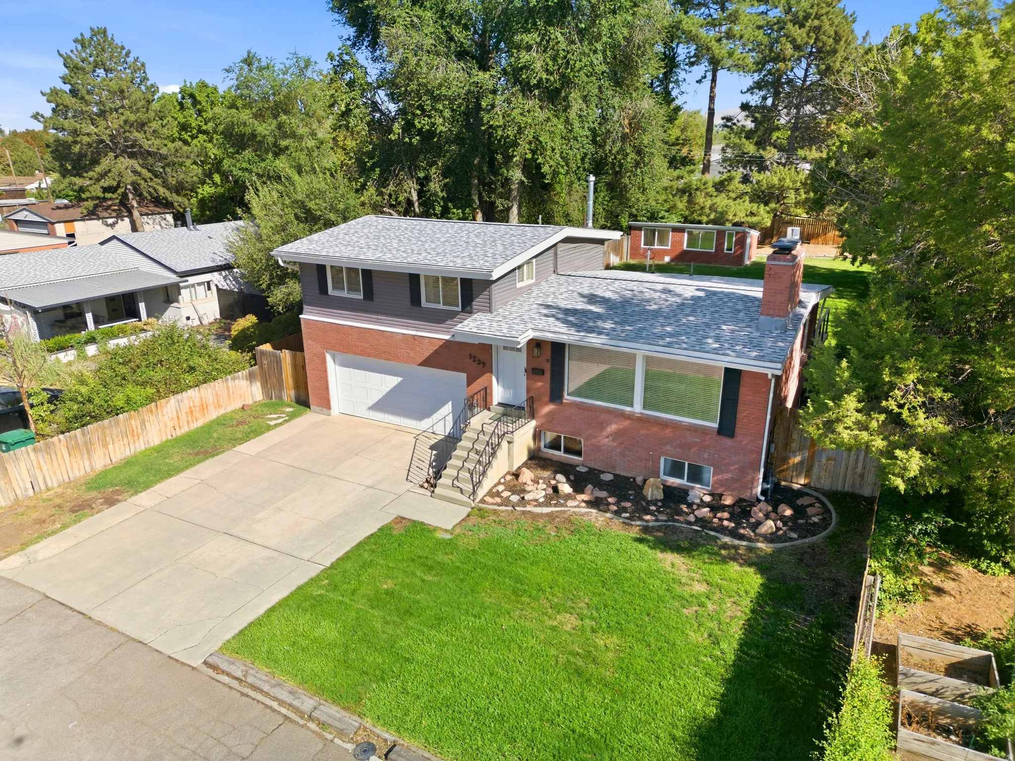 Brick and siding exterior with a shingled roof, featuring a concrete driveway, attached garage, and a landscaped front yard with mature trees