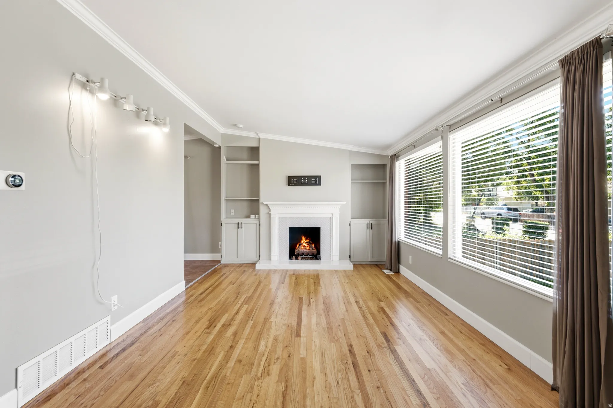 Hardwood flooring, white fireplace with mantel, built-in shelving, built-in cabinetry, and multiple windows