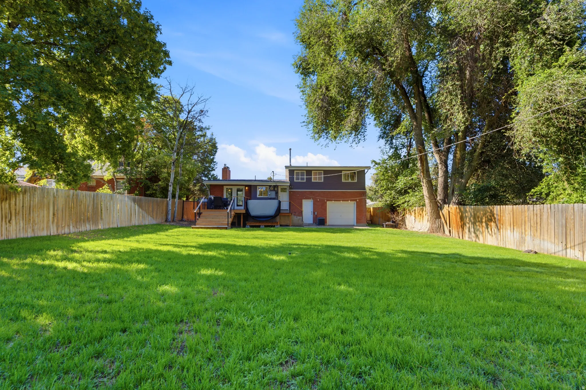 Expansive backyard featuring a manicured lawn, mature trees, wood fence, and a multi-level wood deck