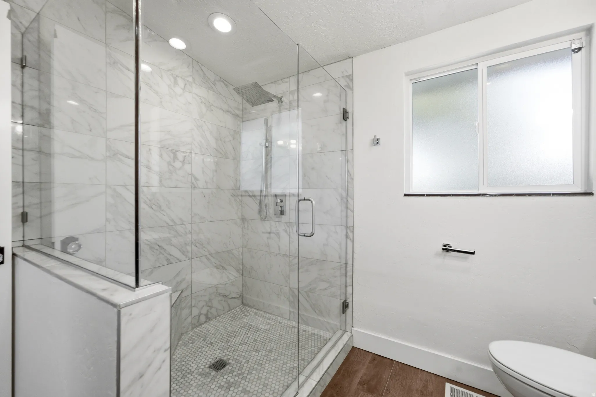 Glass-enclosed shower with full tile surround, hex tile shower floor, and a built-in shower bench