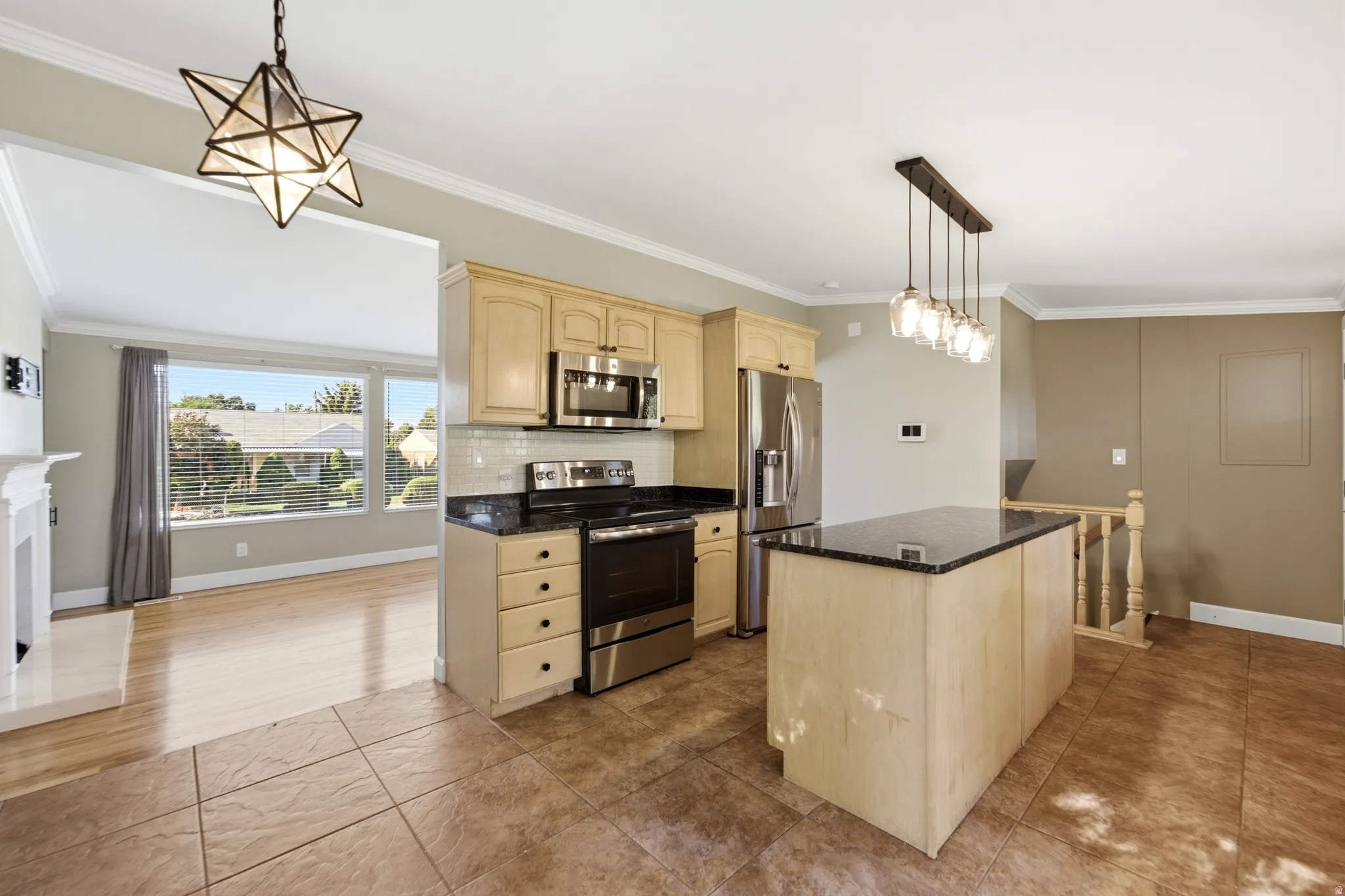Kitchen featuring wood-finish cabinetry, stainless steel appliances, a center island with a dark countertop, and tile flooring