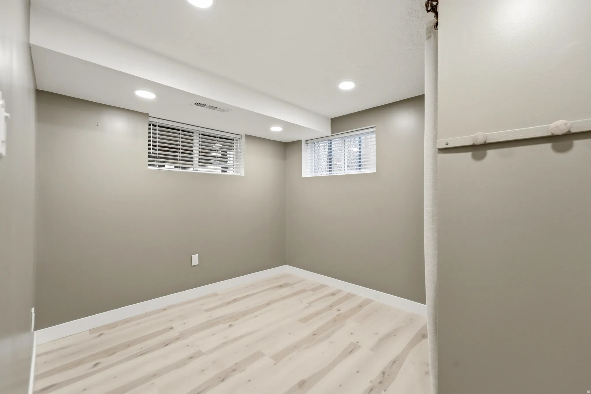 Recessed lighting illumination, light wood-finish flooring, two windows with blinds, and neutral wall paint