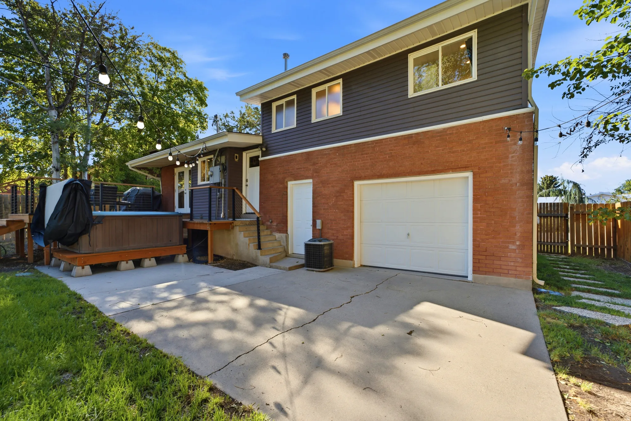 Exterior featuring brick and horizontal siding, an attached garage, a concrete driveway, a raised deck, and a hot tub