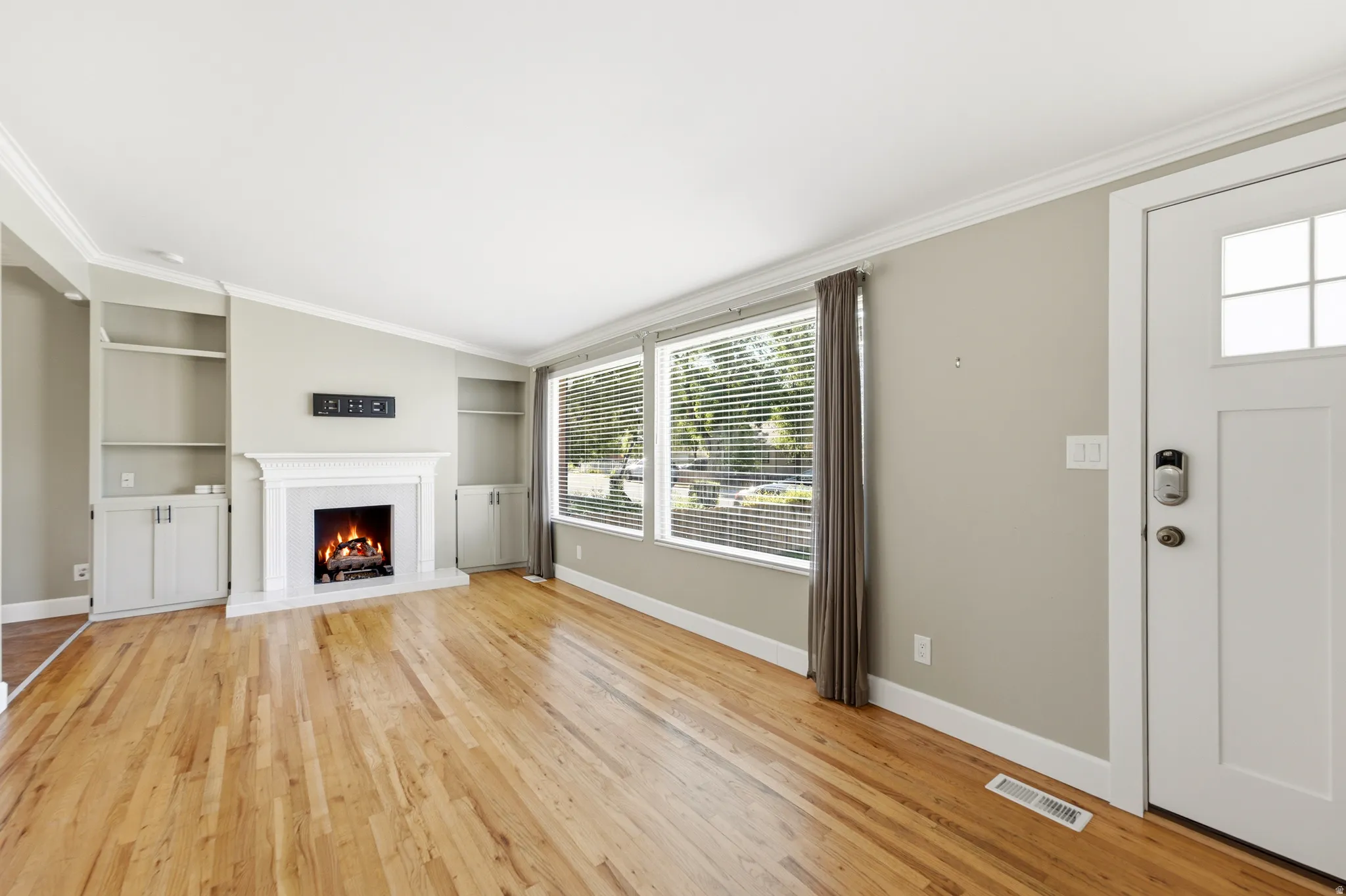 Hardwood flooring, decorative fireplace with mantel, built-in shelving, white trim, and multiple windows