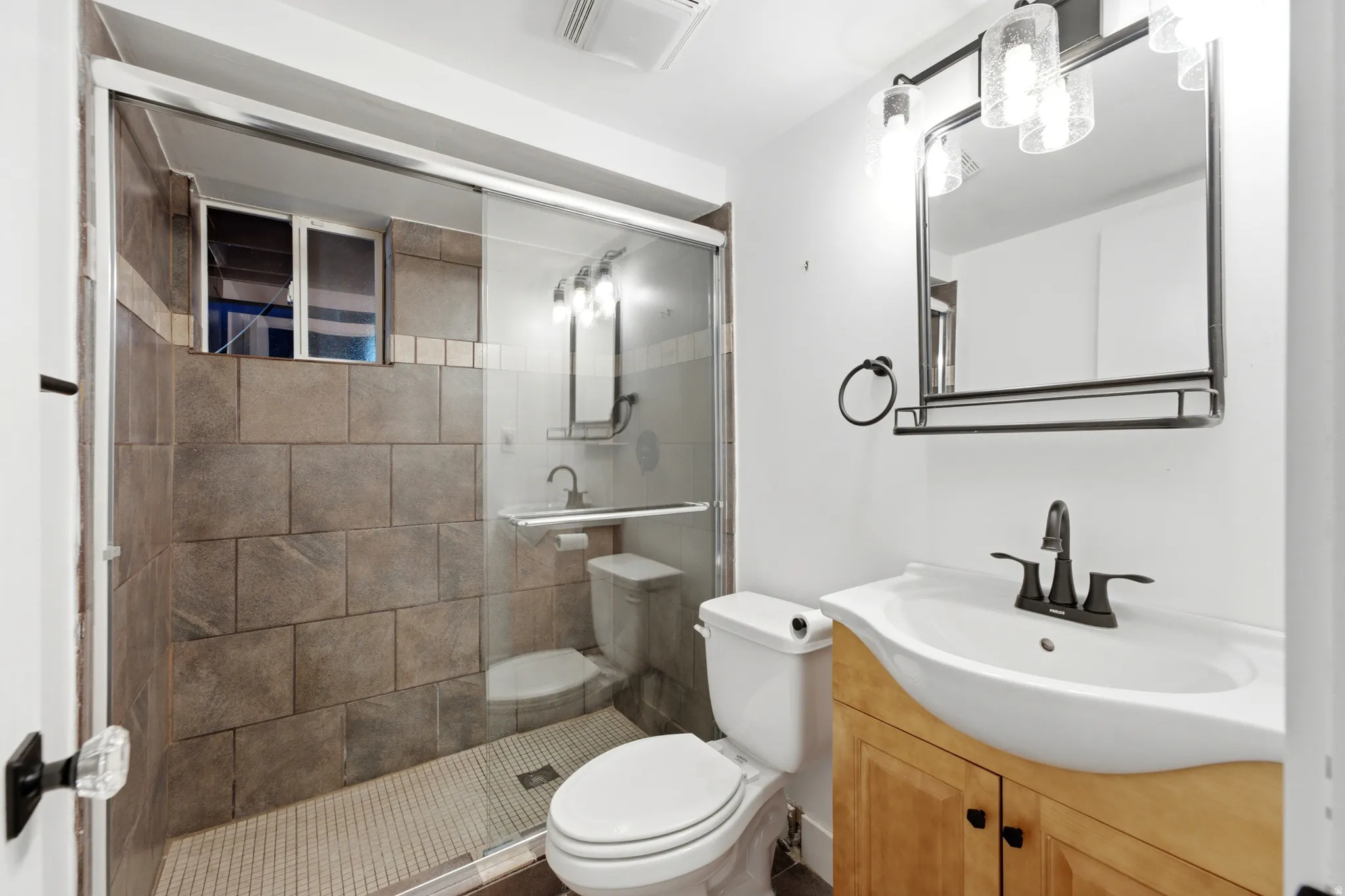 Glass-enclosed shower with tile surround, wood-finish vanity, integrated sink, and modern matte black fixtures