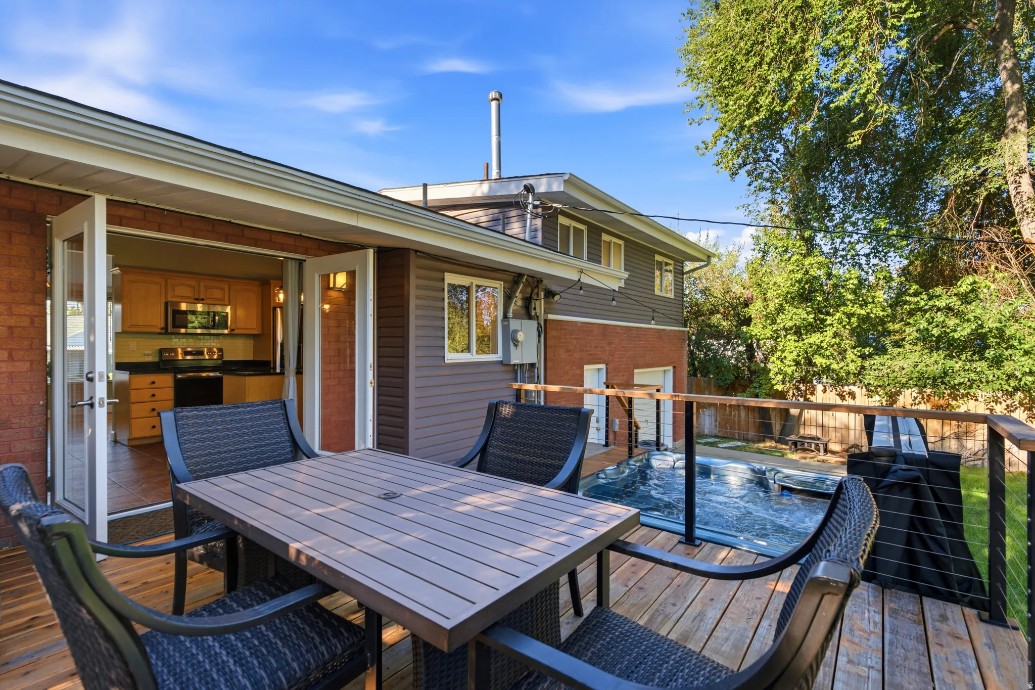 Expansive wood-finish deck with cable railing, providing access to a kitchen with wood cabinetry