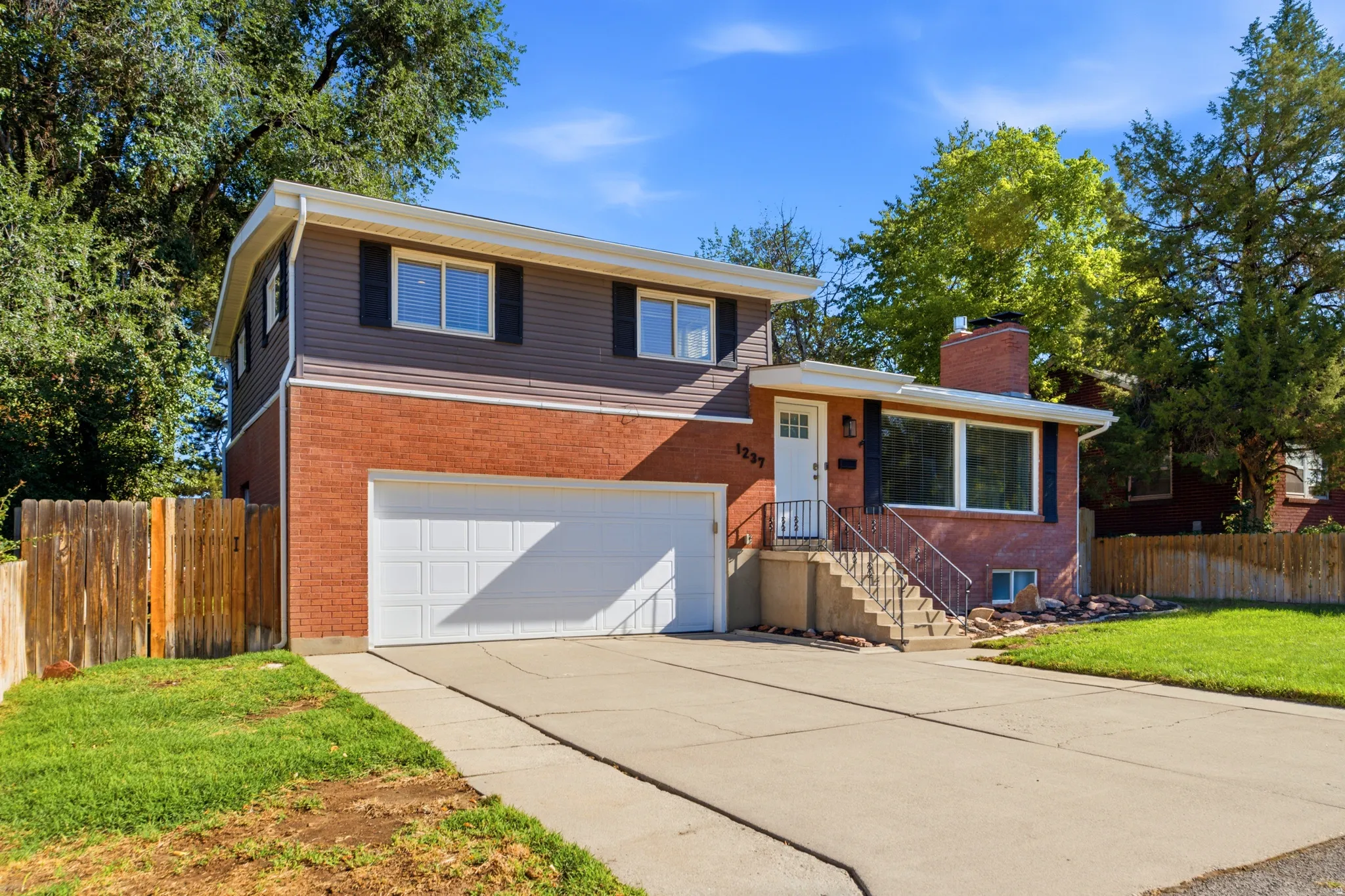 Two-story residence featuring a brick and siding exterior, an attached garage, a paved driveway, and mature landscaping
