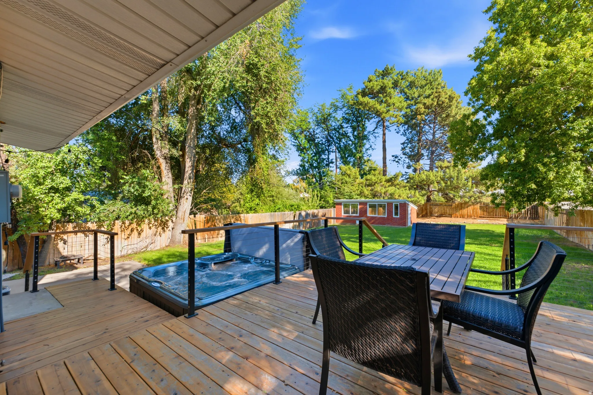 Expansive wood deck with a built-in hot tub, black railing, and a sizable grass yard