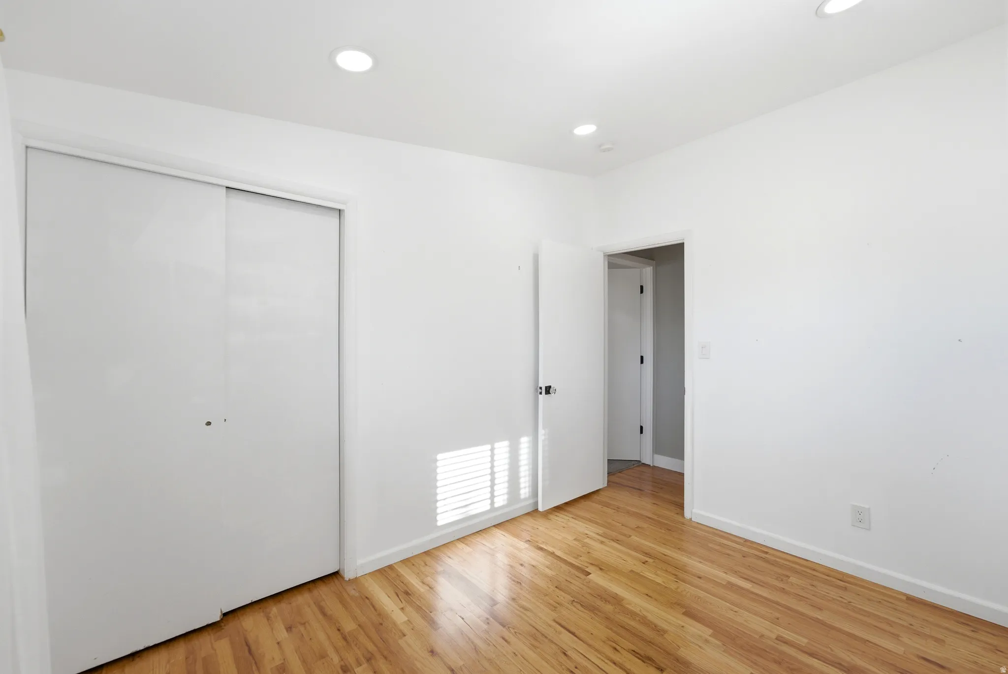 Hardwood flooring, recessed lighting, white walls, and sliding closet doors