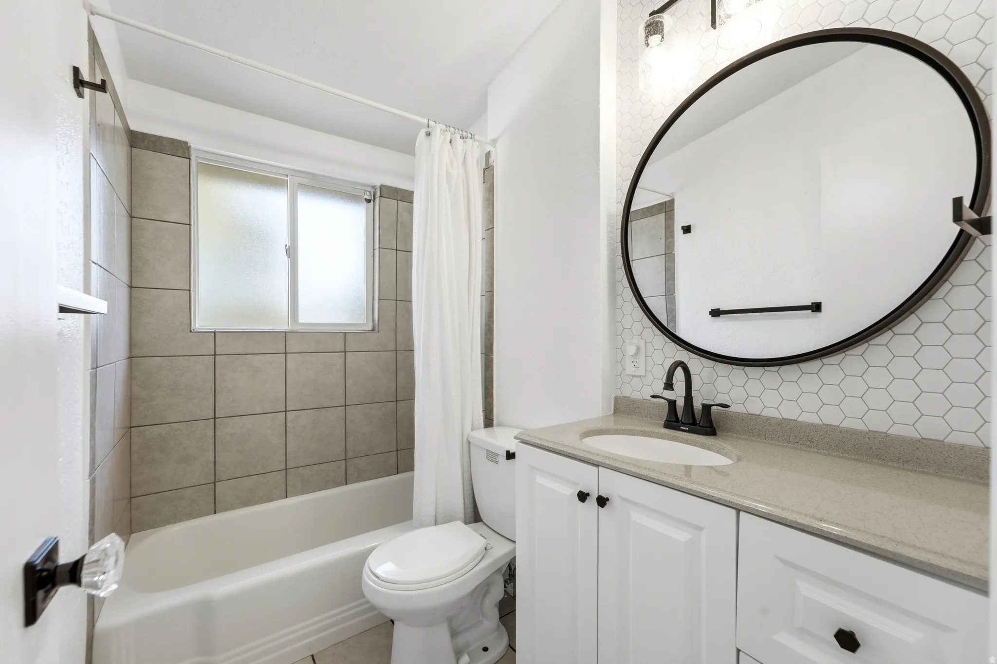 Bathroom featuring a white vanity with a light-toned countertop, a round black-framed mirror, a black wall-mounted faucet, and a tiled shower-bath combination
