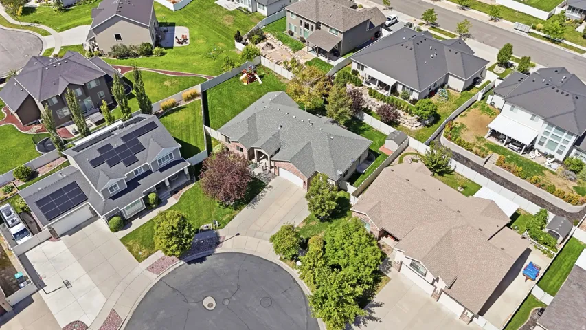 Aerial view of residential homes featuring solar panels, landscaped yards, and paved driveways