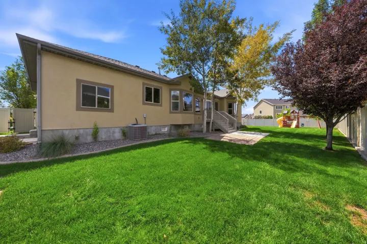 Expansive green lawn, mature trees, stucco exterior, multi-paned windows, and a paved patio area