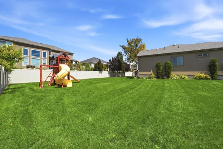 Spacious backyard featuring a manicured lawn, full privacy fencing, and mature landscaping