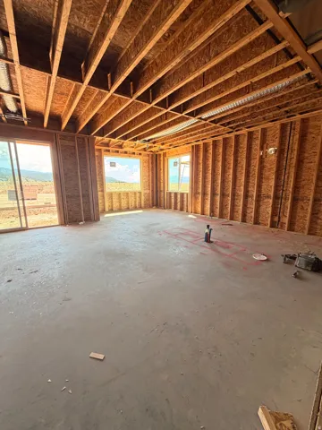Spacious room featuring exposed wood framing, concrete subfloor, and multiple window openings