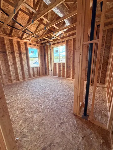 Unfinished interior framing with exposed wood studs, two double-hung windows, and ceiling trusses