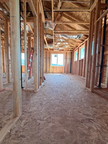 Unfinished interior framing with exposed ceiling joists, wood subflooring, and multiple window openings