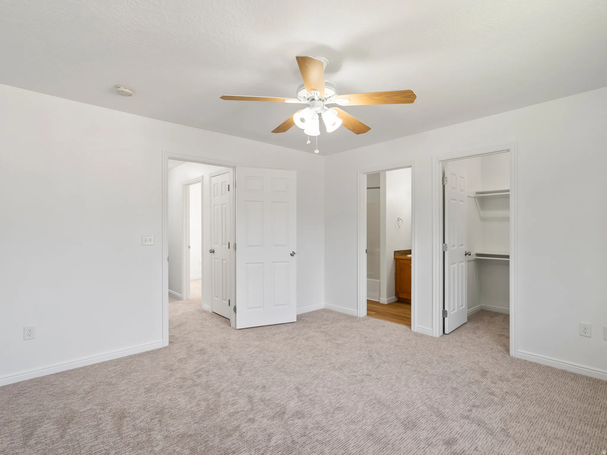 Neutral carpet flooring, white painted walls, ceiling fan with light fixture, paneled interior doors, and a built-in closet with shelving