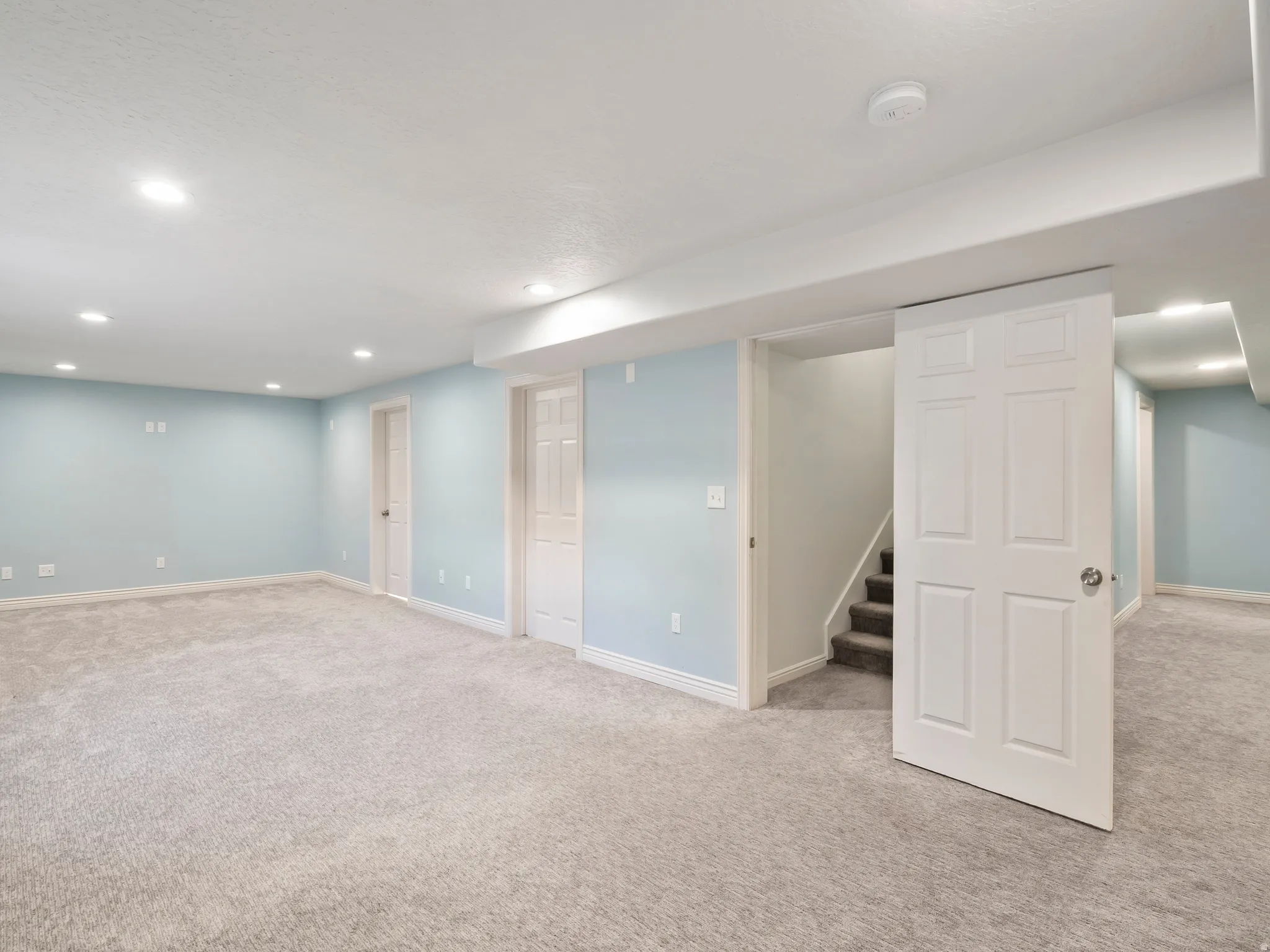 Expansive room featuring light blue walls, plush carpeting, multiple recessed lighting fixtures, and white paneled doors