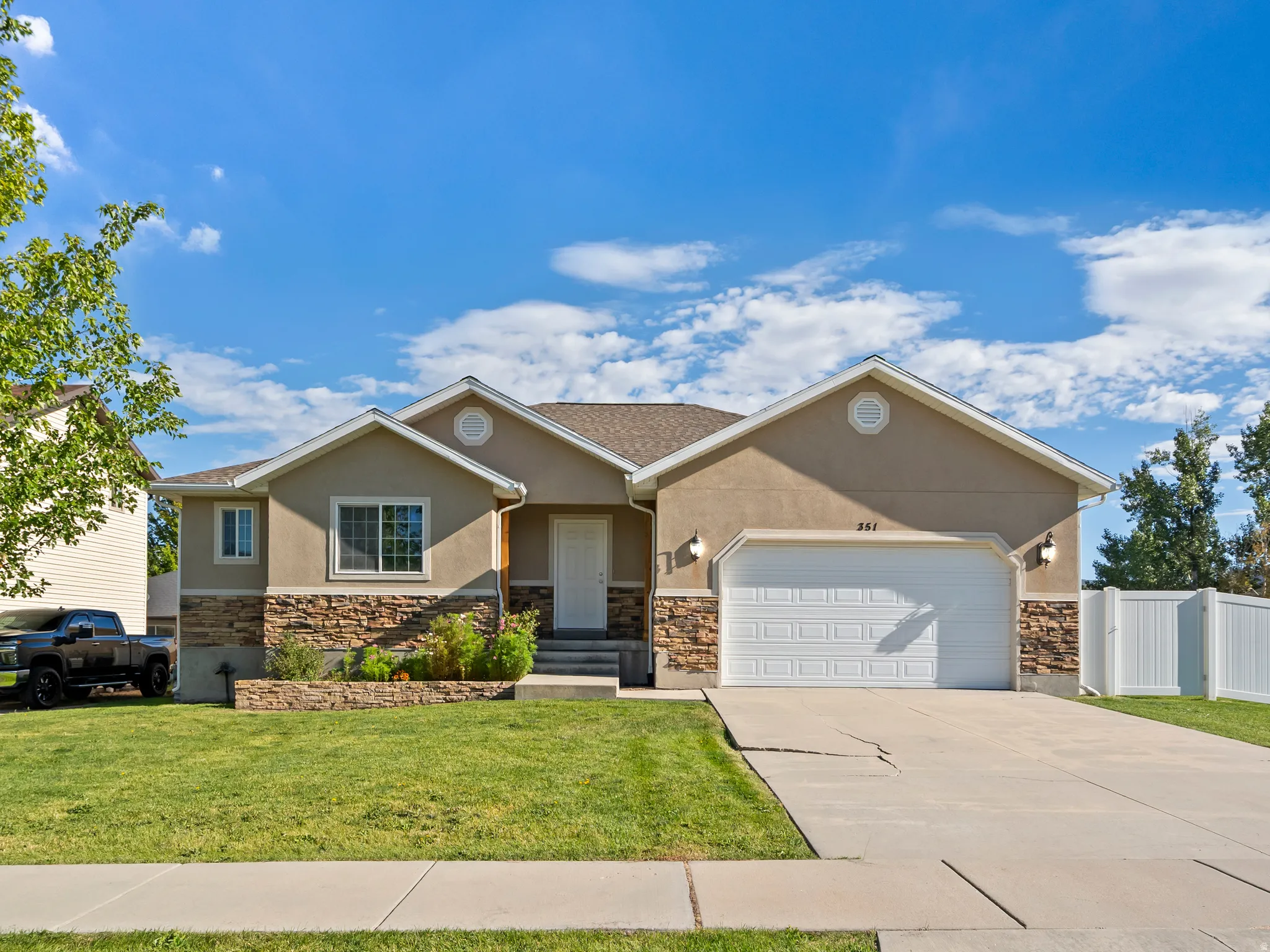 Stucco exterior with stone veneer accents, integrated garage, white privacy fencing, and a manicured lawn