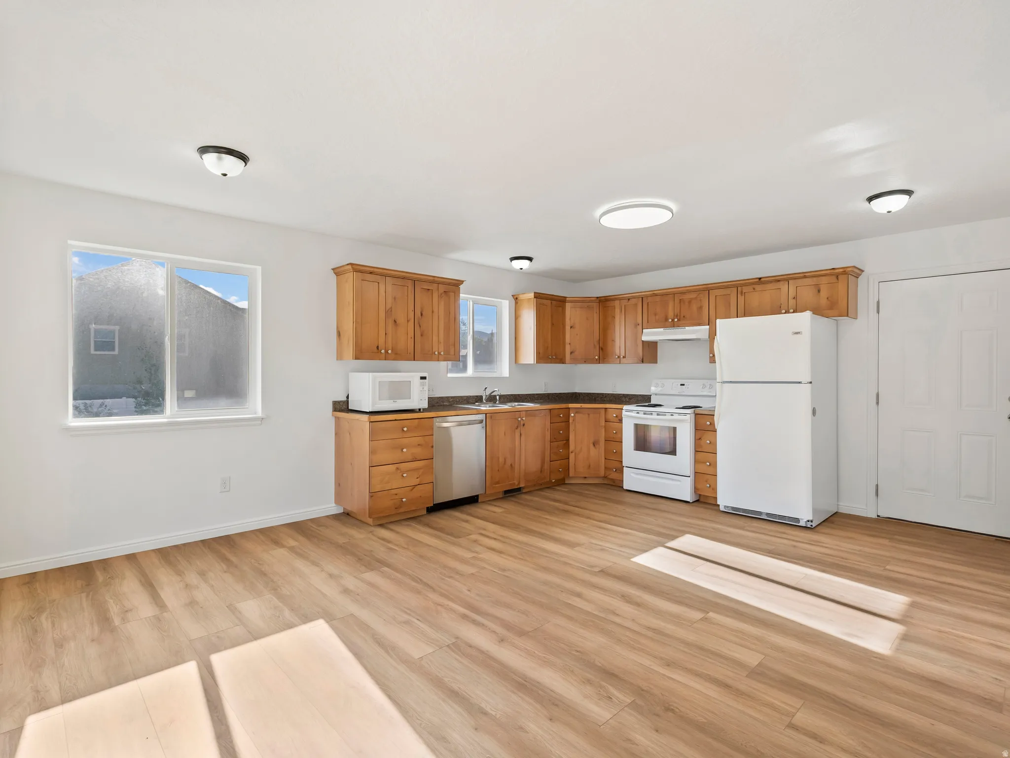 Wood-finish flooring throughout, white walls, and a U-shaped kitchen featuring wood cabinetry, integrated appliances, and a double window