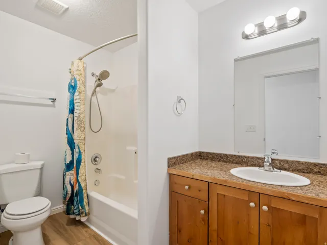 Bathroom featuring a wood-finish vanity with a built-in sink, a speckled countertop, a mirrored wall, a three-light vanity fixture, and a shower-over-tub combination