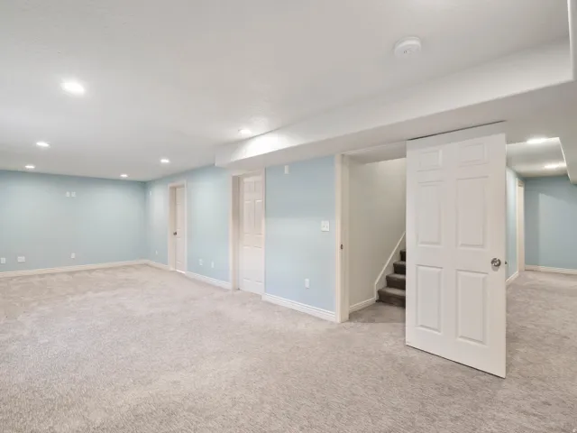 Expansive room featuring light blue walls, plush carpeting, multiple recessed lighting fixtures, and white paneled doors