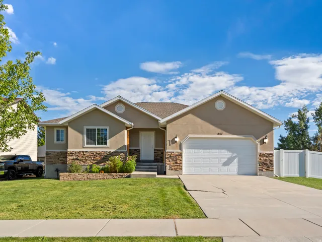 Stucco exterior with stone veneer accents, integrated garage, white privacy fencing, and a manicured lawn