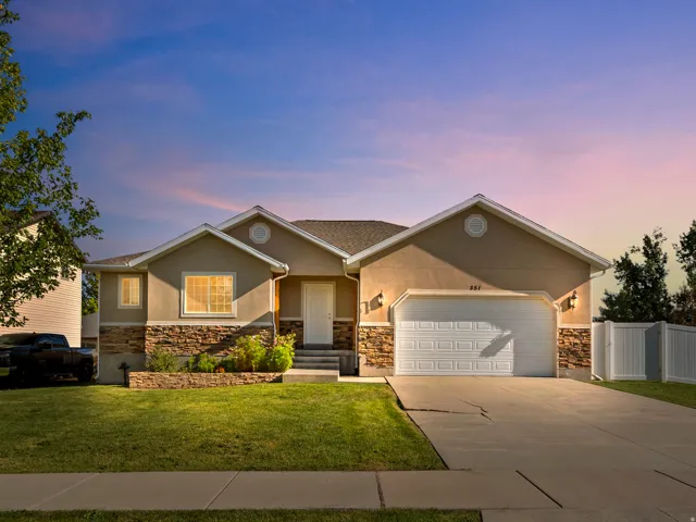 Stucco exterior with stone accenting, attached two-car garage, white privacy fence, and manicured front lawn