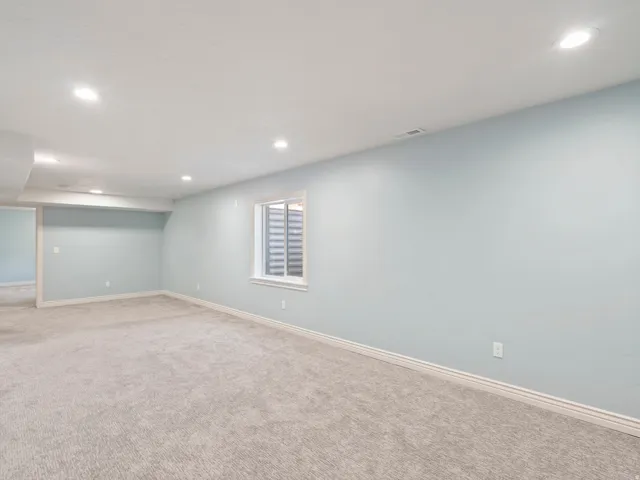 Recessed lighting, light-toned carpeting, single window with a white frame, and light blue wall finish