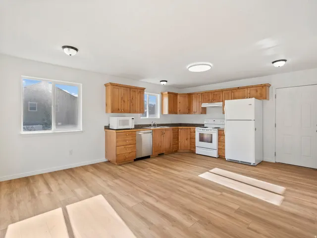 Wood-finish flooring throughout, white walls, and a U-shaped kitchen featuring wood cabinetry, integrated appliances, and a double window