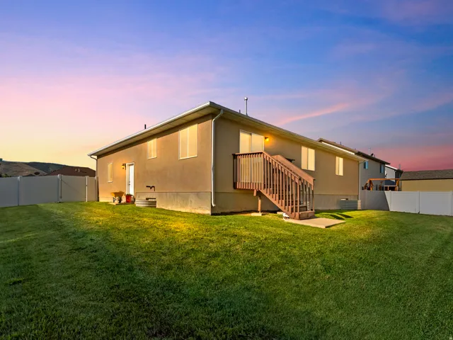 Expansive backyard featuring a manicured lawn, full vinyl privacy fencing, and an exterior wood deck with stairs