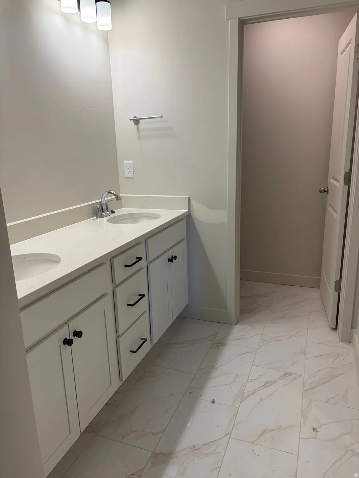 Dual vanity with under-mount sinks, light-toned countertop, white cabinetry with black hardware, and patterned tile flooring