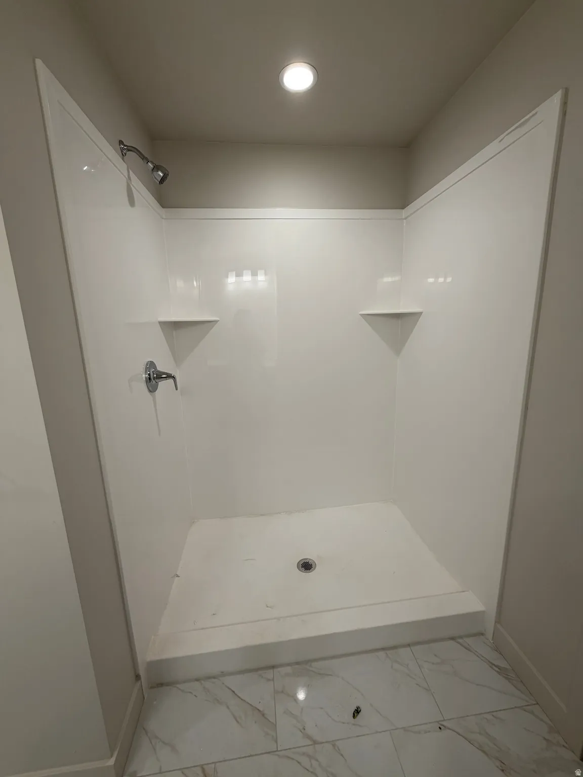 White shower enclosure with integrated corner shelving, chrome fixtures, and recessed ceiling lighting