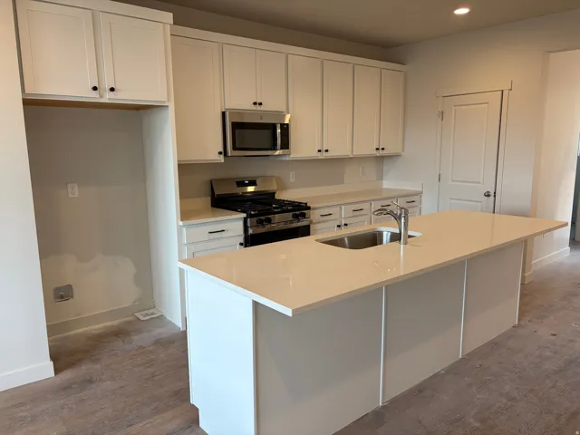 White shaker-style cabinetry, stainless steel microwave, gas range, light-toned countertops, and wood-finish flooring