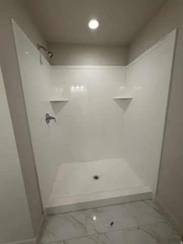 White shower enclosure with integrated corner shelving, chrome fixtures, and recessed ceiling lighting