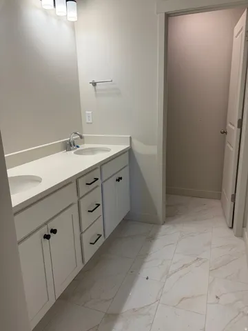 Dual vanity with under-mount sinks, light-toned countertop, white cabinetry with black hardware, and patterned tile flooring