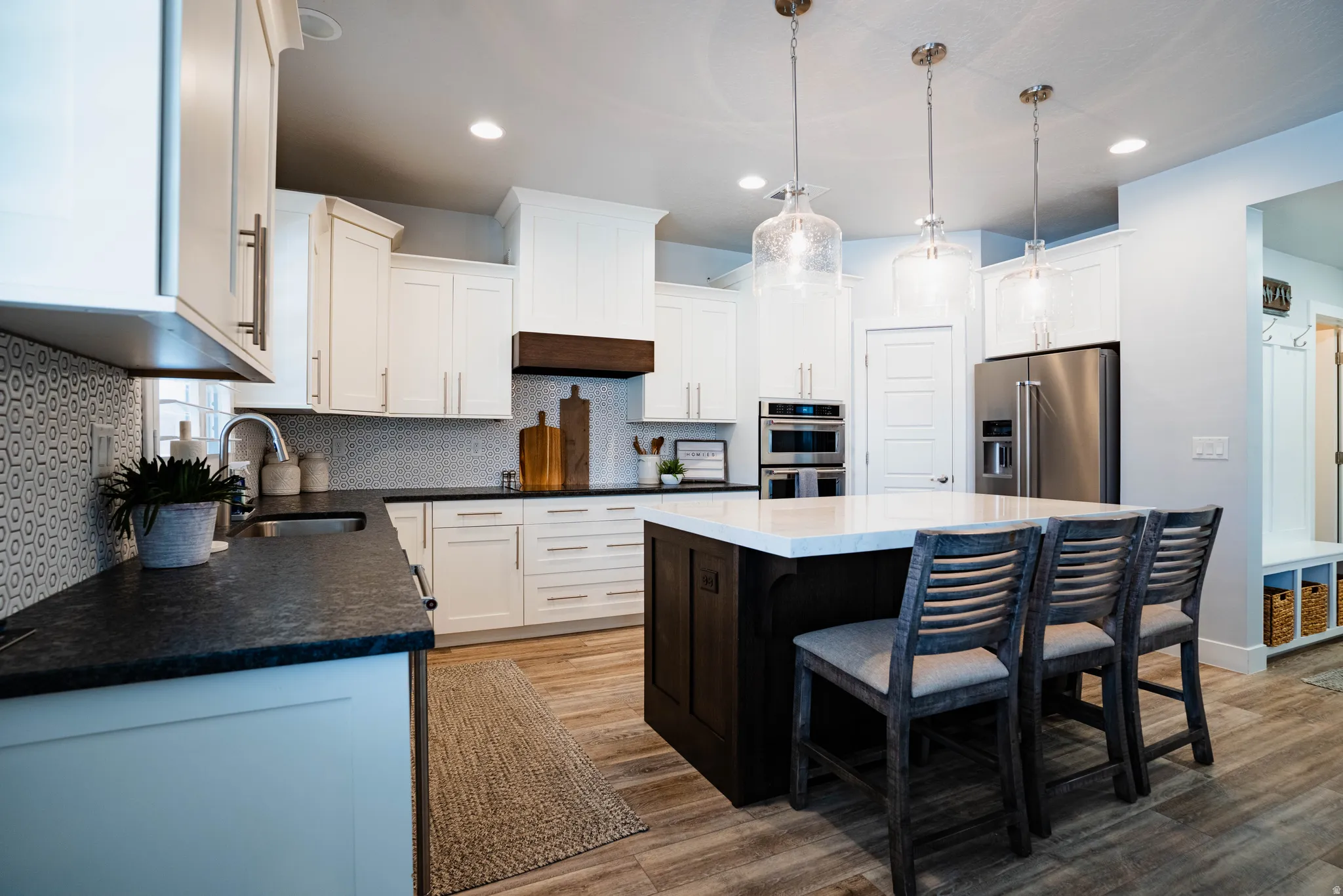 White cabinetry, black countertops, stainless steel appliances, wood-finish flooring, and pendant lighting