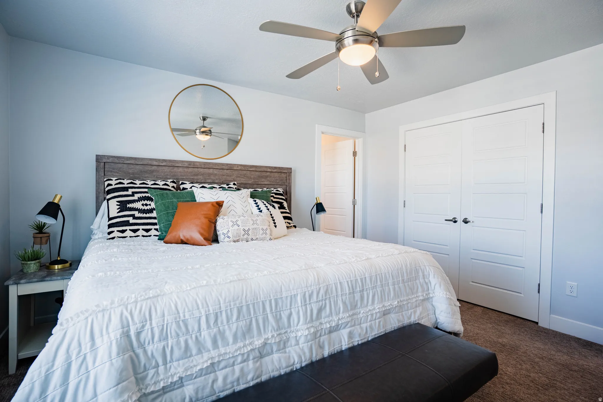 Ceiling fan with integrated lighting, wood-finish headboard, textured carpet flooring, double-door closet with horizontal paneling, and an interior door
