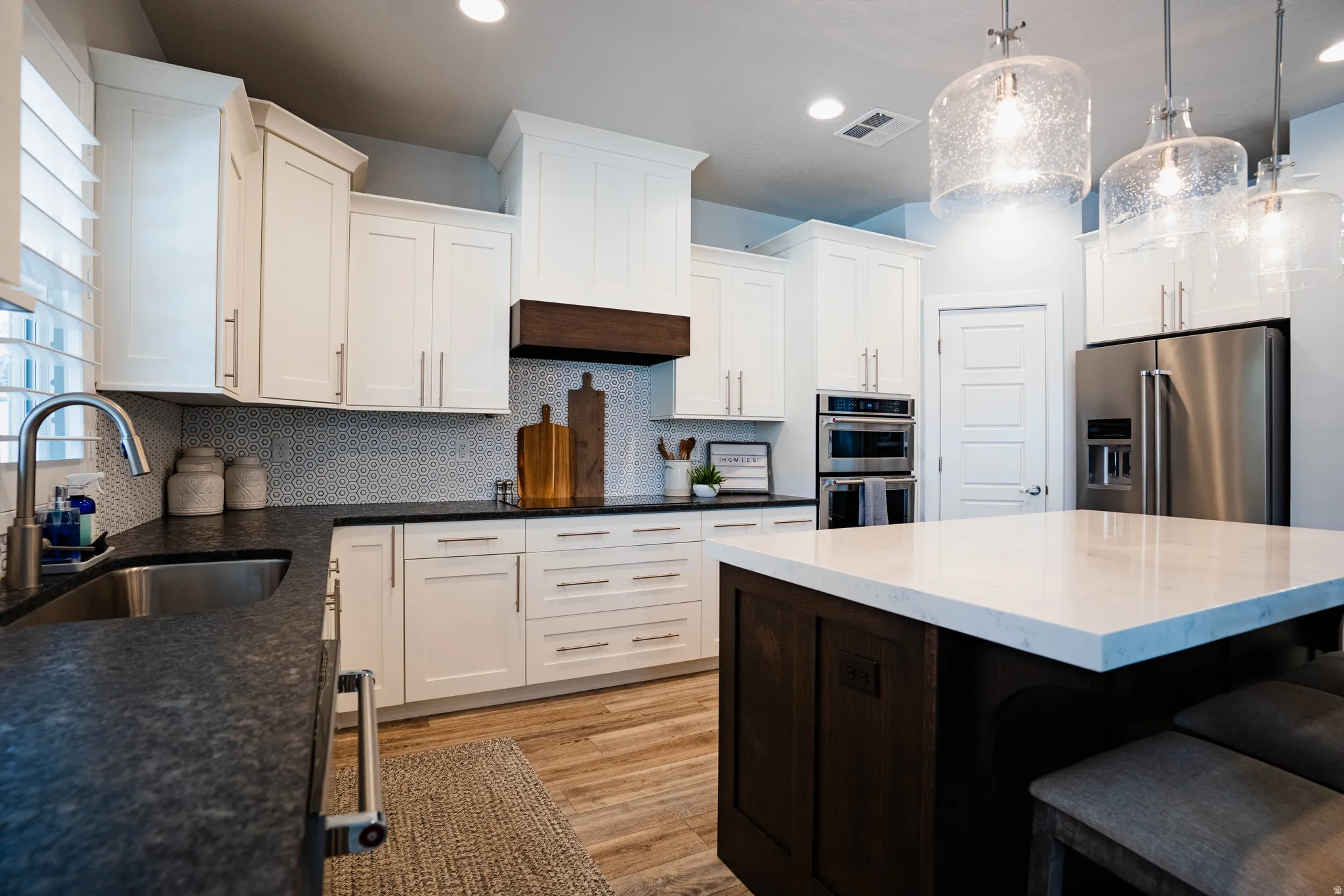 Gourmet kitchen featuring white cabinetry, dark stone countertops, stainless steel appliances, a center island with light-colored countertop, and wood-finish flooring