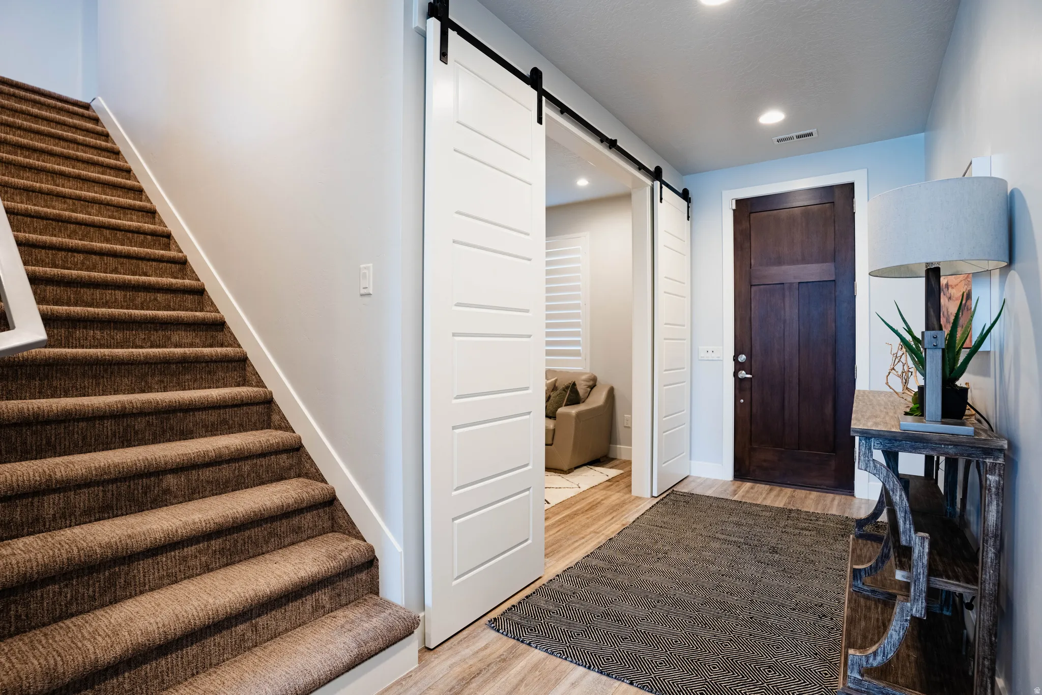 Staircase with carpeted treads, wood-finish flooring, white barn doors, and a paneled dark wood entry door